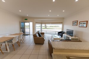 Una habitación amplia con zona de comedor, sofá, televisor y un gran ventanal con vistas al exterior.