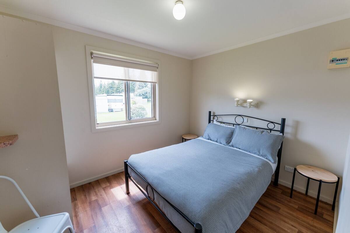 Une chambre à coucher avec un lit, une fenêtre, une table de chevet et un petit tabouret.