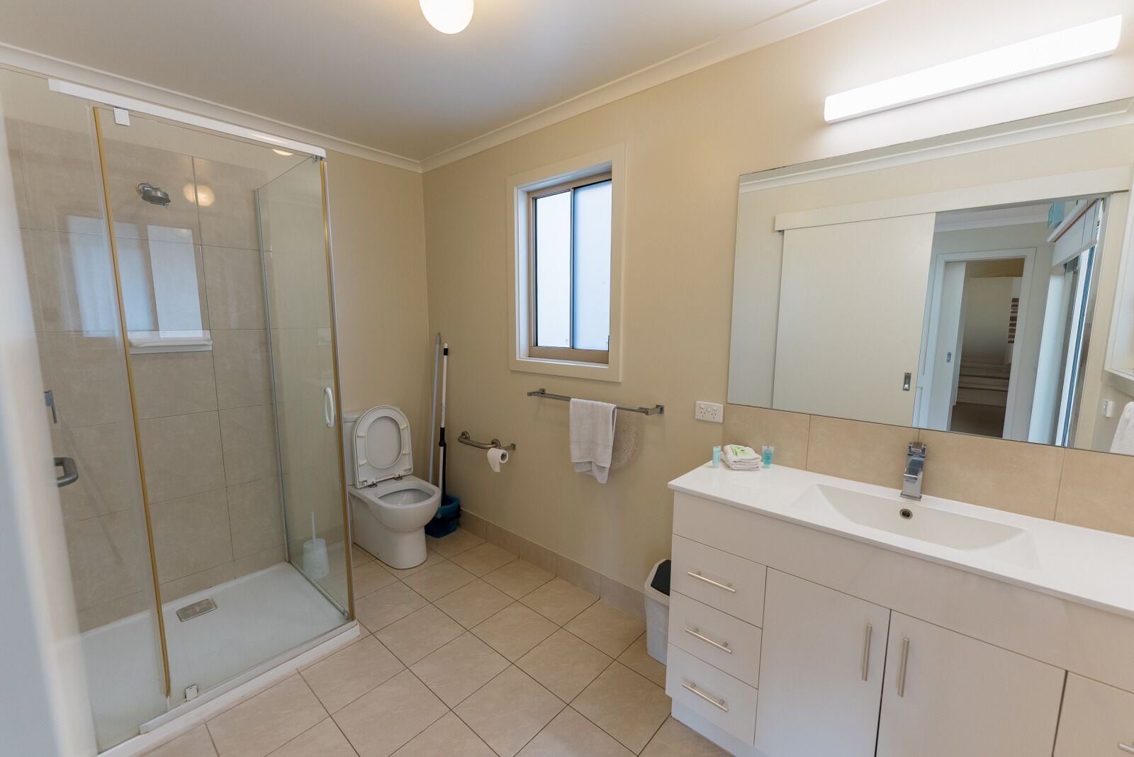 A bathroom with a glass shower enclosure, a toilet, a sink with a mirror, and a window.