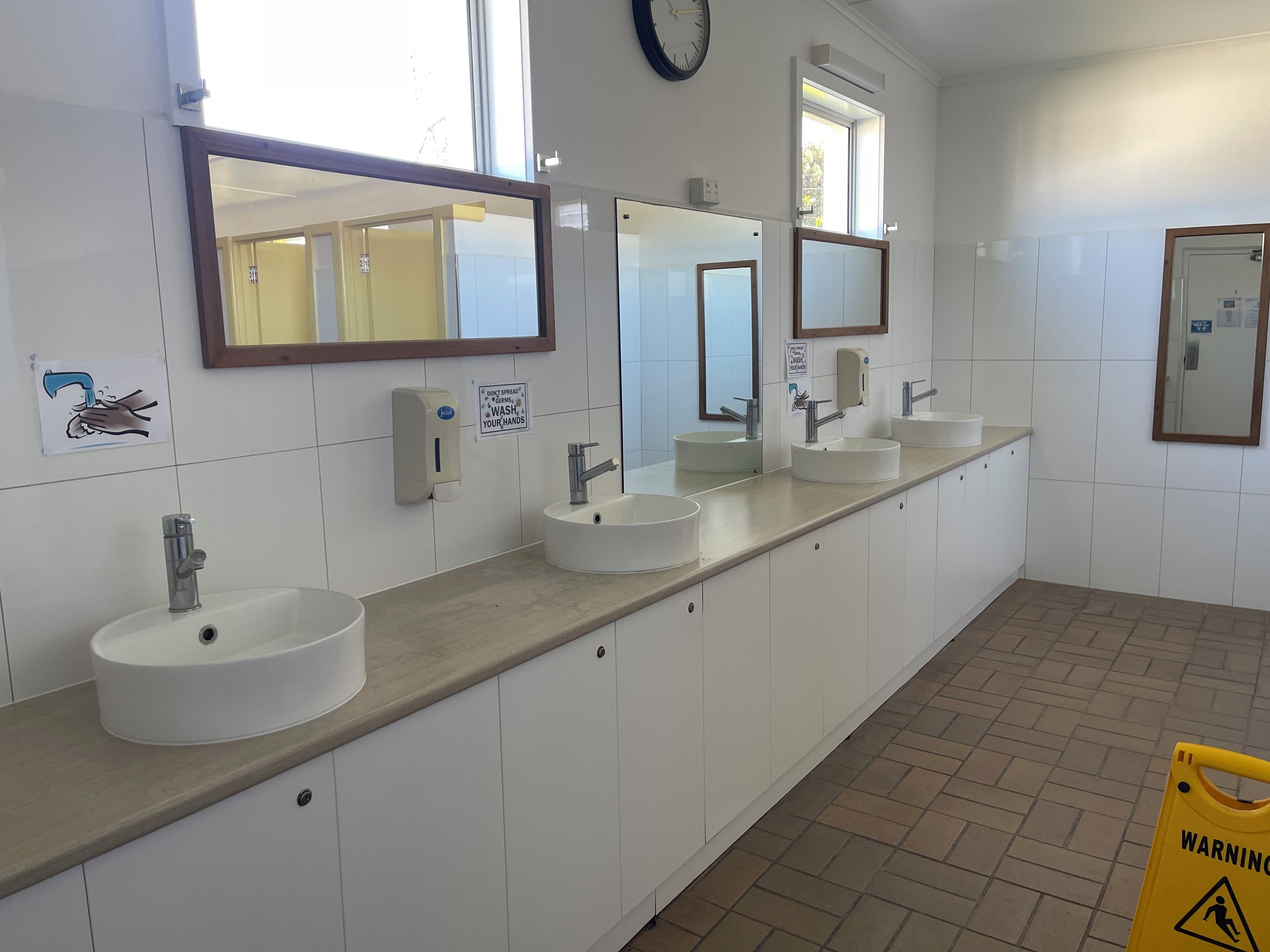 A public restroom with three sinks, hand dryers, and mirrors.