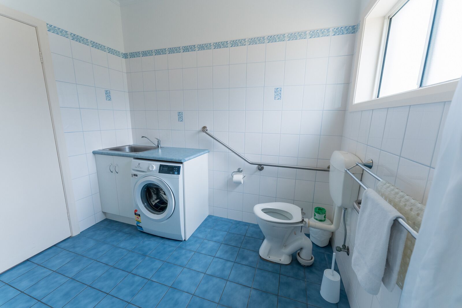 Et lille, rent badeværelse med vaskemaskine, toilet og et vindue.