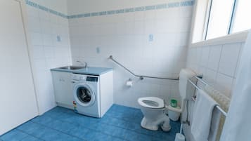Et lille, rent badeværelse med vaskemaskine, toilet og et vindue.