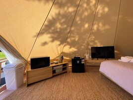 Una carpa con cama, televisor, hervidor y un refrigerador pequeño.