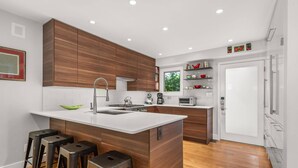 Eine moderne Küche mit Holzausstattung, einer zentralen Kochinsel mit Barhocker und einer weißen Arbeitsplatte.