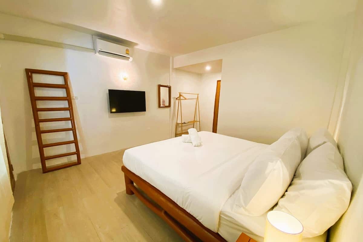 Une chambre avec un lit en bois, un téléviseur à écran plat fixé au mur, une échelle en bois et une table de chevet avec une lampe.