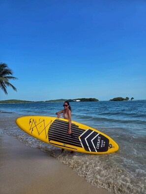 A person holding a yellow paddleboard with black and white designs on a beach. - Ubox samui Hostel & Bungalows (Koh Samui)