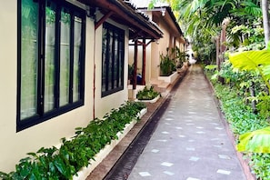 A corridor with a tiled floor, a planter with green plants, and a building with large windows. - Ubox samui Hostel & Bungalows (Koh Samui)
