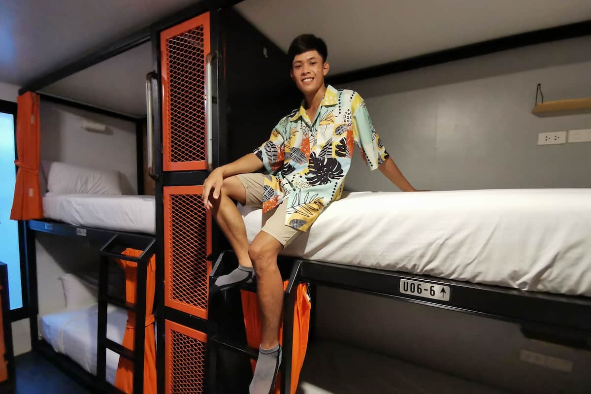 Une chambre avec un lit superposé aux barreaux orange, et une personne assise sur le lit du haut.