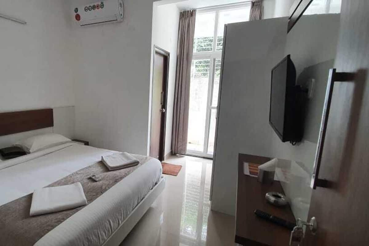 A hotel room with a bed, a bedside table, a TV, and a door leading to a balcony.