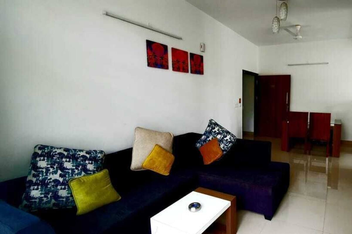 A living room with a sofa, a coffee table, and a TV. There are wall decorations and a door leading to another room.