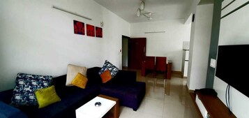 A living room with a sofa, a coffee table, and a TV. There are wall decorations and a door leading to another room.