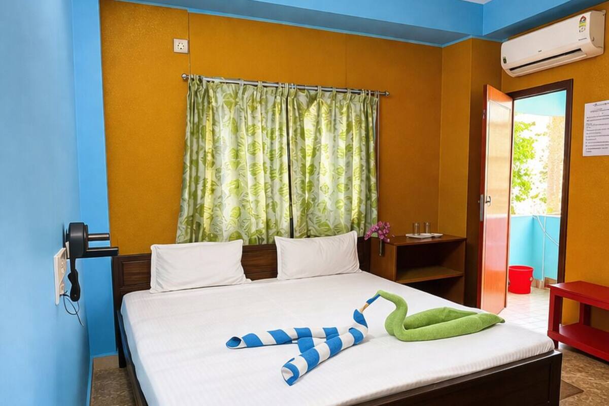 A bedroom with a bed, a ceiling fan, an air conditioning unit, and a window with curtains.