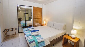 A hotel room with a bed, bedside table, lamp, and a wooden bench.