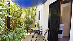 A small patio area with a table and chairs, surrounded by potted plants and a black mesh door.