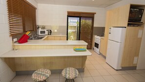 Una cucina compatta con forno a microonde, fornello e frigorifero. Sono presenti due sgabelli e un'isola piccola con un forno a microonde e una moka.