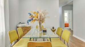 A dining area with a glass table, yellow chairs, and a vase with dried flowers. - Work & Play: Colorful Home in Heart of NOLA! (New Orleans)
