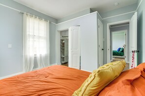 A bedroom with an orange bedspread, a yellow pillow, and a closet with hanging clothes. - Work & Play: Colorful Home in Heart of NOLA! (New Orleans)