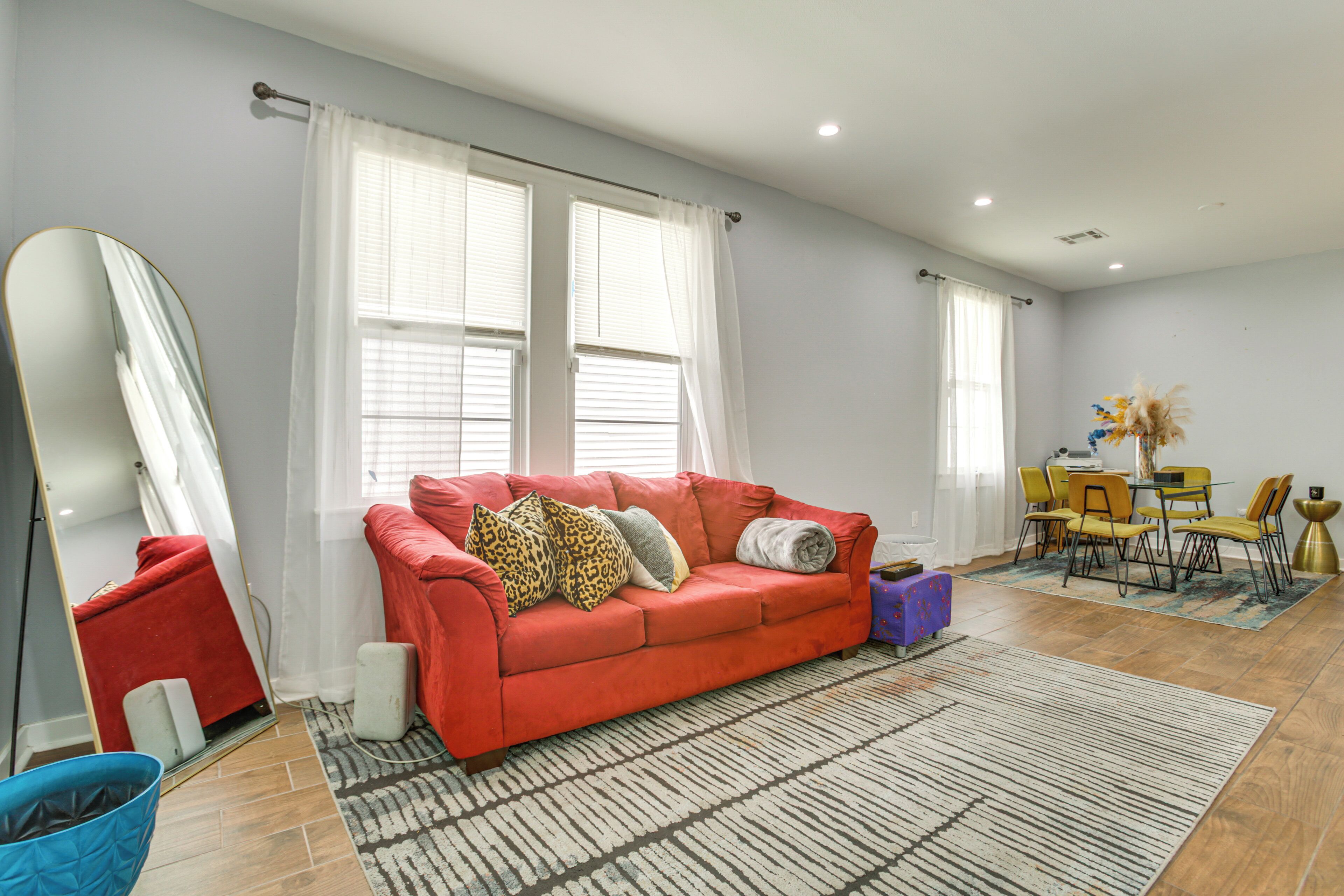 A living room with a red sofa, a large mirror, a dining table with chairs, and a patterned rug.