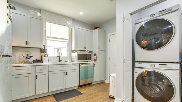 A modern kitchen with white cabinets, a dishwasher, a microwave, and a stacked washer and dryer. - Work & Play: Colorful Home in Heart of NOLA! (New Orleans)