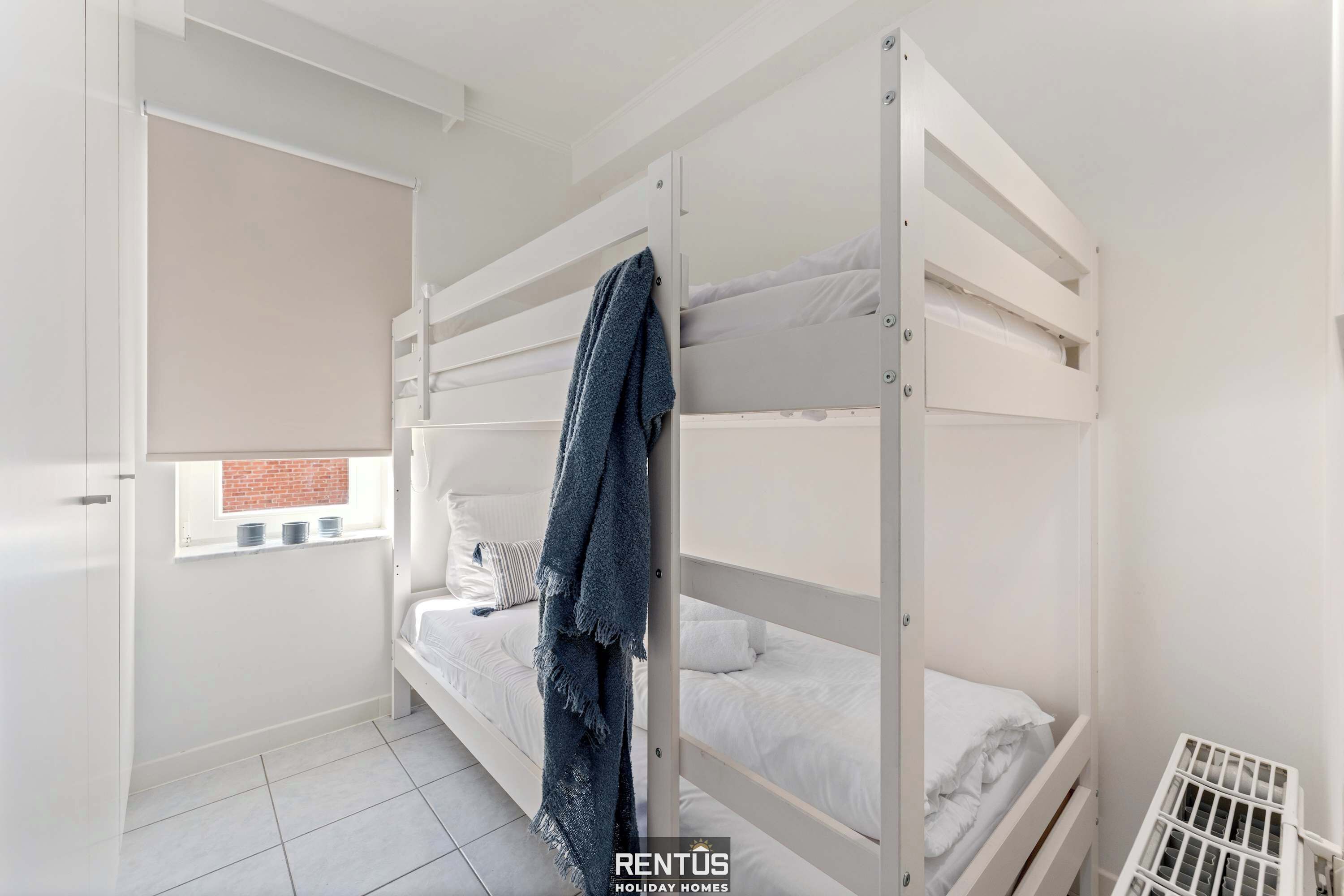 A compact room with bunk beds, a small window with blinds, and a radiator.