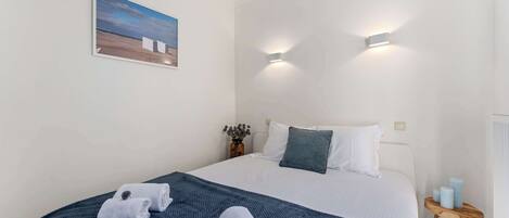Ein Schlafzimmer mit einem Bett, zwei Wandleuchten, einem Gemälde, einem kleinen Tisch mit Kerzen und einer blauen Decke.
