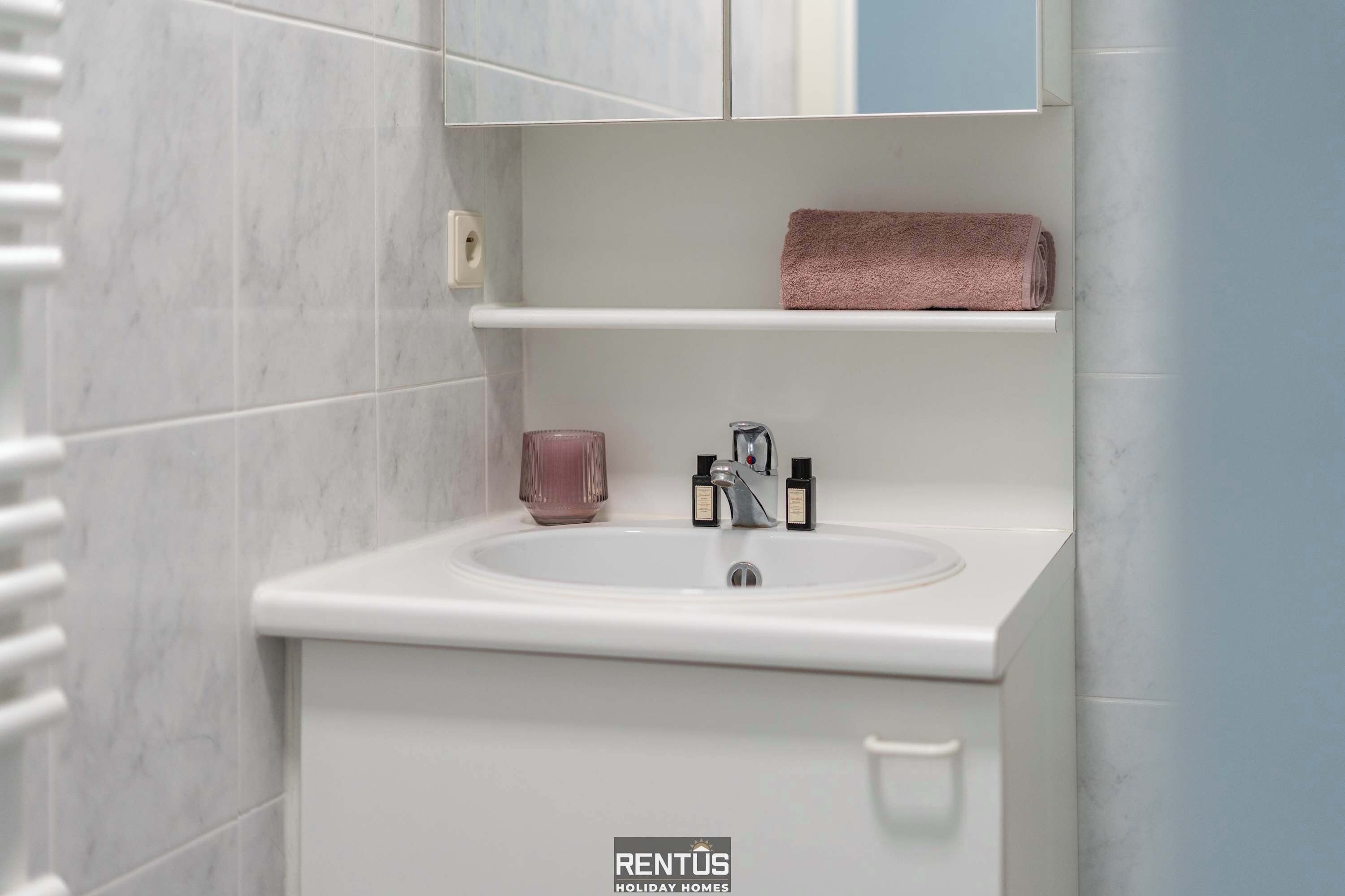 A bathroom with a white sink, a pink towel, and a bottle of shampoo.
