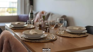 A dining table set with plates, bowls, and wine glasses, with a bottle and a vase on the table.