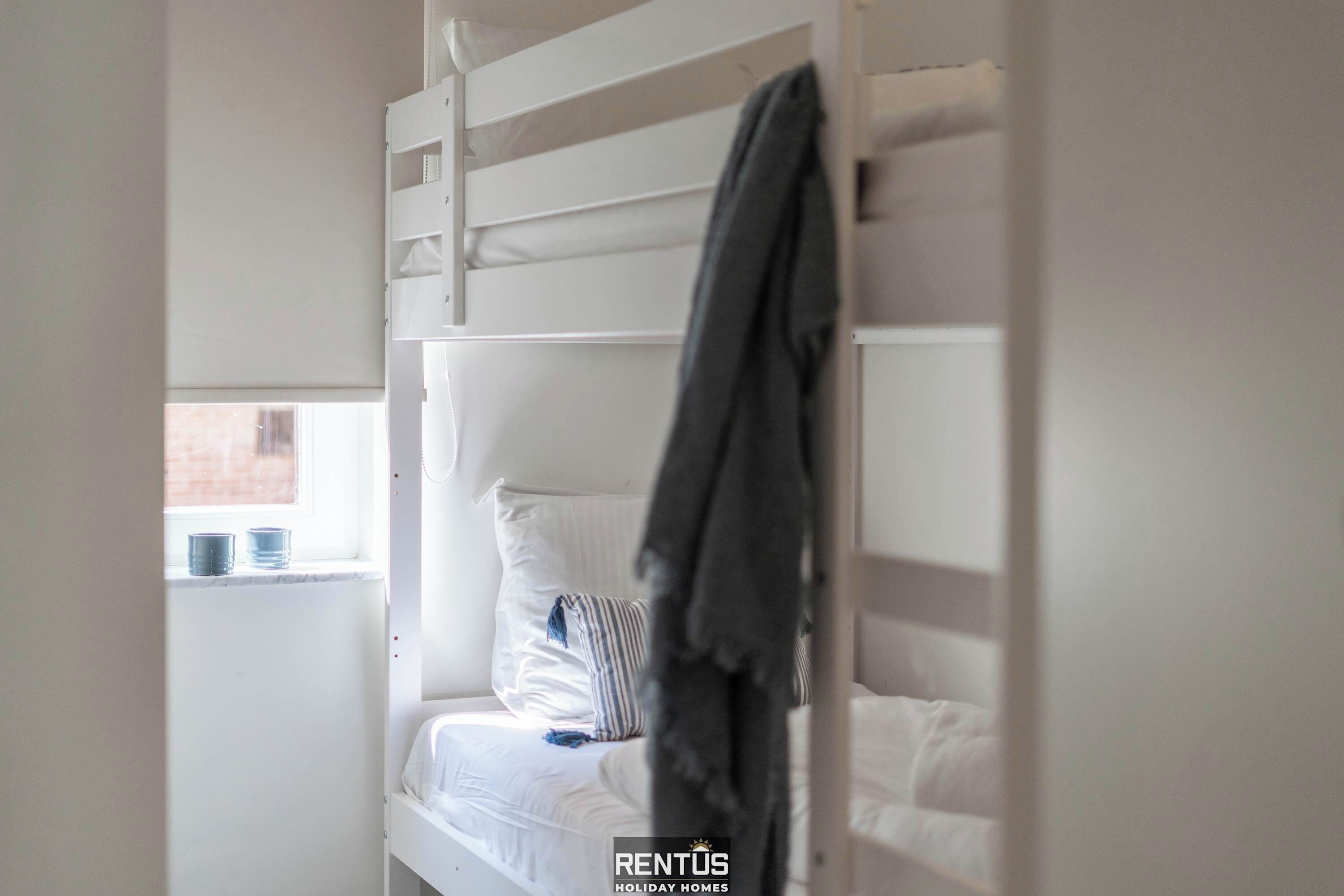 Ein Etagenbett mit aufgehängtem Handtuch, ein Fenster mit Blick auf ein Backsteinhaus und ein Schild für RENTUS Holiday Homes.
