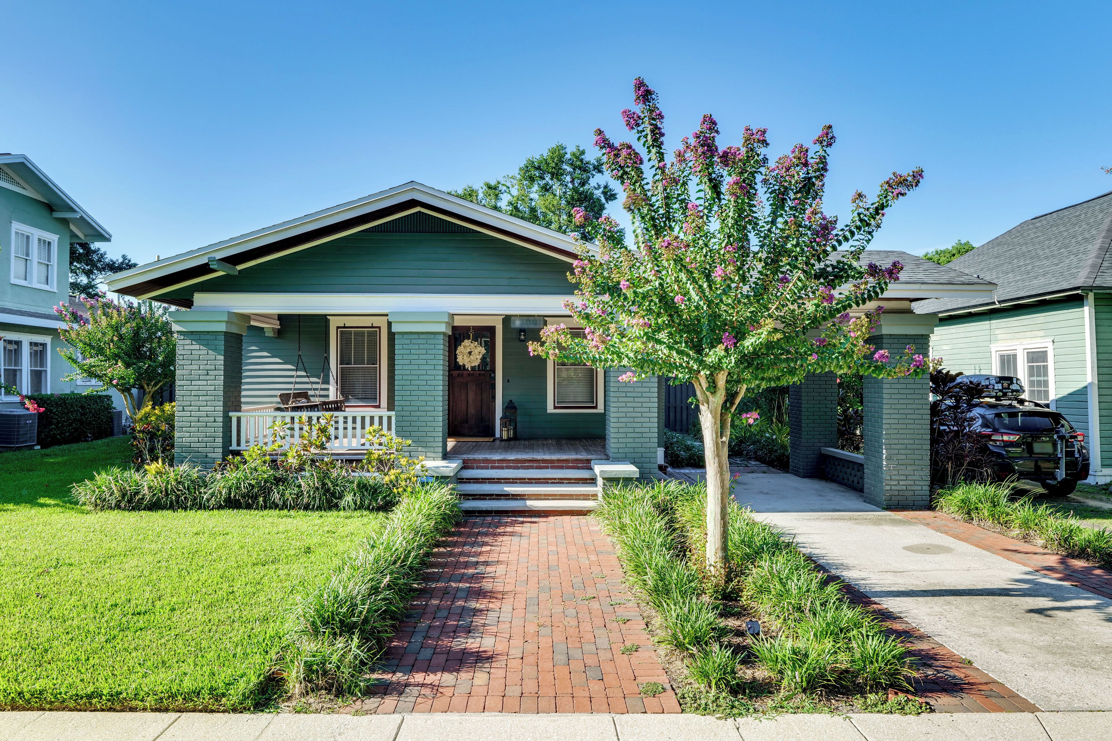 A two-story house with a front porch, a brick pathway leading to the entrance, and a tree with pink flowers.