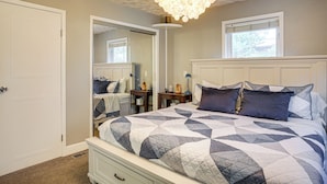 A bedroom with a large bed, a nightstand, a dresser, a mirror, and a chandelier.