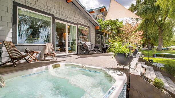 A hot tub in a backyard with a brick house, outdoor furniture, and a large umbrella.