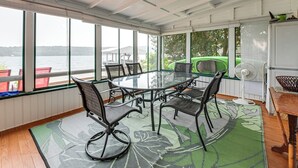 Een overdekt eetgedeelte buiten, met een glazen tafel en stoelen, een ventilator en uitzicht op het water.