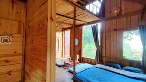 A wooden cabin room with a bed, a small table, and a window with curtains. - To Chim Ri Homestay Mang Đen (Mang Den)