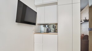 Een kleine keuken met witte kastjes, een ingebouwde magnetron en een flatscreen televisie aan de muur.