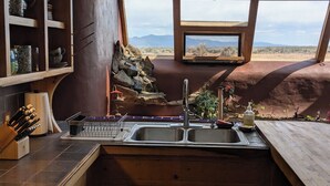 A kitchen with a large window overlooking a desert landscape. - SolShip, An Original Earthship in Tres Piedras (Tres Piedras)