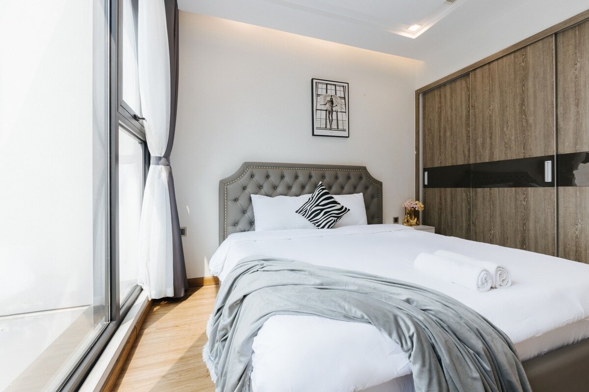 A neatly made bed with a grey headboard, white bedding, and a zebra-patterned pillow. There is a framed picture on the wall above the bed, and a wooden wardrobe to the right.
