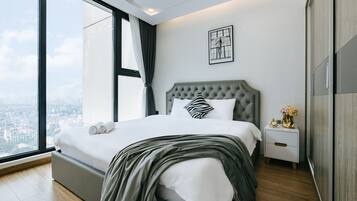 A modern bedroom with a large bed, a nightstand, a framed artwork, and a view of the city through a large window.