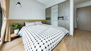 Een moderne slaapkamer met een groot bed, een kamerplantje, een hanglamp en een kledingkast.