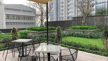 An outdoor patio area with tables and chairs, surrounded by greenery and a view of modern buildings.