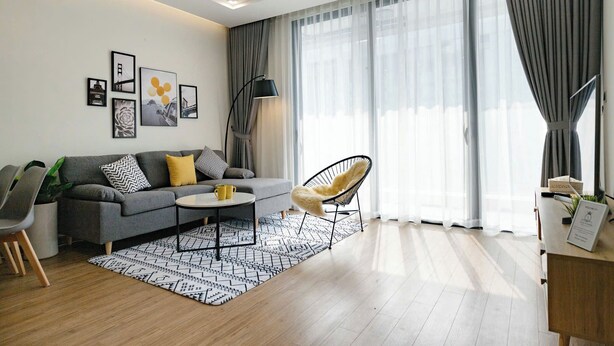 Een moderne woonkamer met een grijze bank, een zwarte fauteuil, een salontafel en een kamerkleed met een patroon.