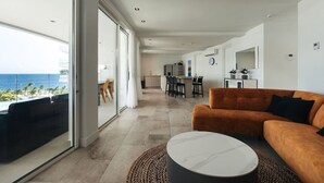 Un salon moderne avec une grande fenêtre, un canapé, une table basse et un coin cuisine à l’arrière-plan.
