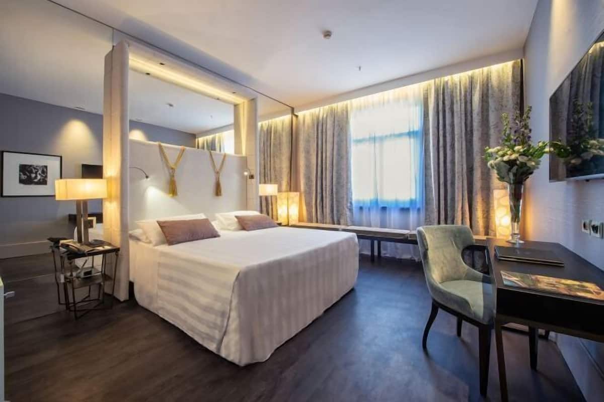 Hotellihuone, jossa on suuri sänky, yöpöydät, työpöytä ja tuoli.