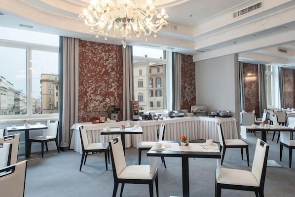 A hotel dining area with tables and chairs, a chandelier, and large windows. - Sina Bernini Bristol, Autograph Collection (Rome)
