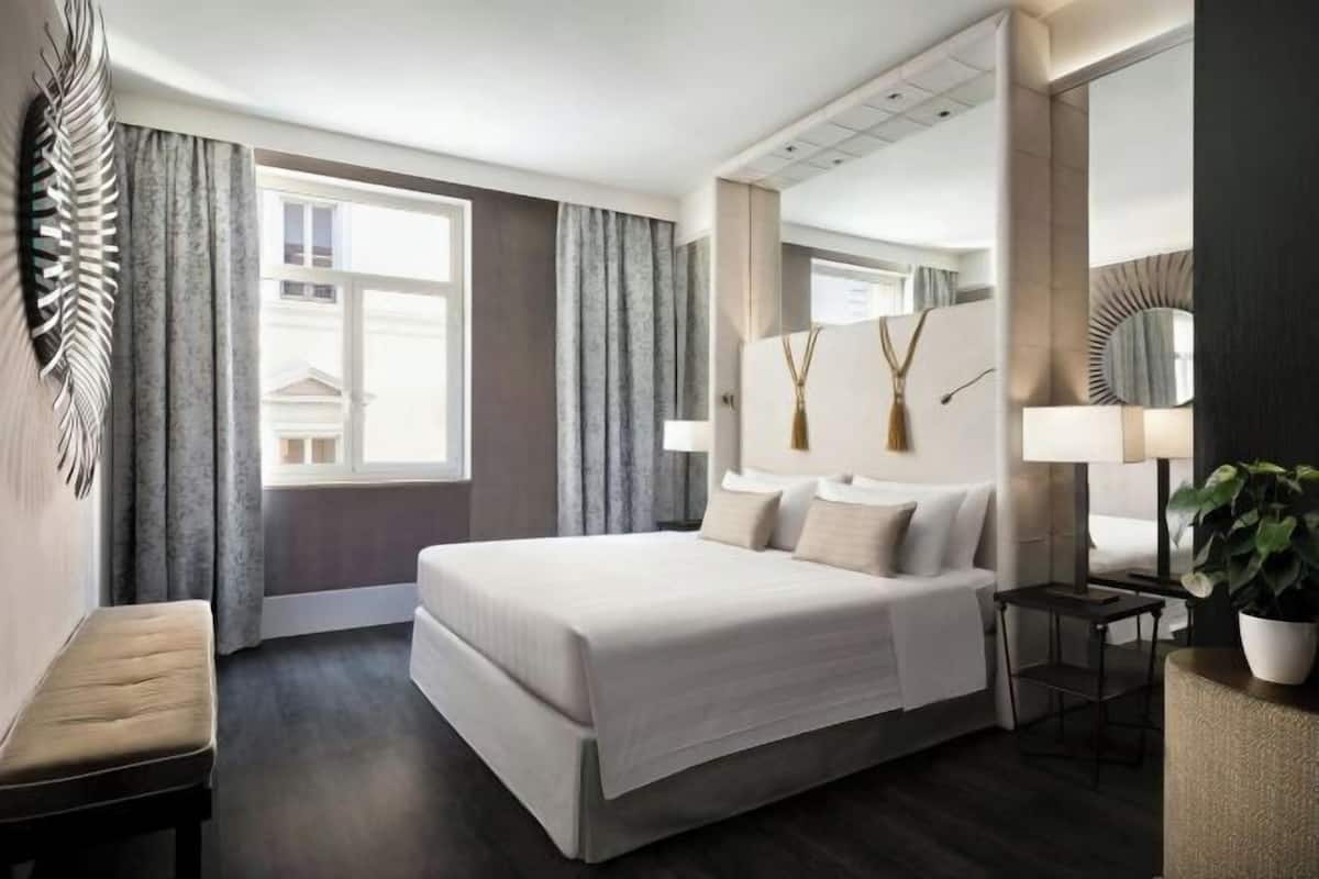 Moderni hotellihuone, jossa on suuri sänky, yöpöytä, tuoli, peili ja ruukussa oleva kasvi.
