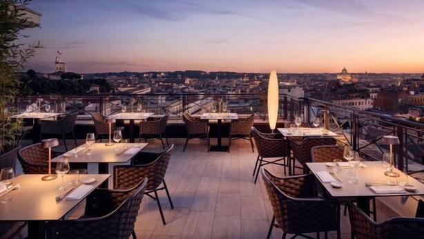 An outdoor dining area with tables and chairs, overlooking a cityscape during sunset. - Sina Bernini Bristol, Autograph Collection (Rome)