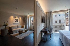 A modern hotel room with a sofa, a desk, a bed, and a large window offering a city view. - Sina Bernini Bristol, Autograph Collection (Rome)
