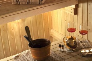 A wooden sauna with a copper pot, a ladle, and two glasses of red liquid on a mat. - Sina Bernini Bristol, Autograph Collection (Rome)