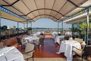 An outdoor terrace with tables and chairs, a covered roof, and a view of the city. - Sina Bernini Bristol, Autograph Collection (Rome)