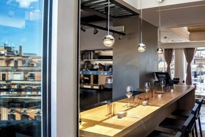 A modern bar area with a wooden counter, hanging pendant lights, and a view of the cityscape. - Sina Bernini Bristol, Autograph Collection (Rome)