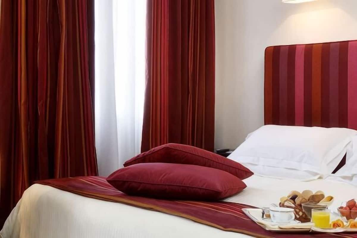 Hotellihuone, jossa on sänky, punaiset verhot, tarjotinalus aamiaisruokien kanssa ja raidallinen pääty.
